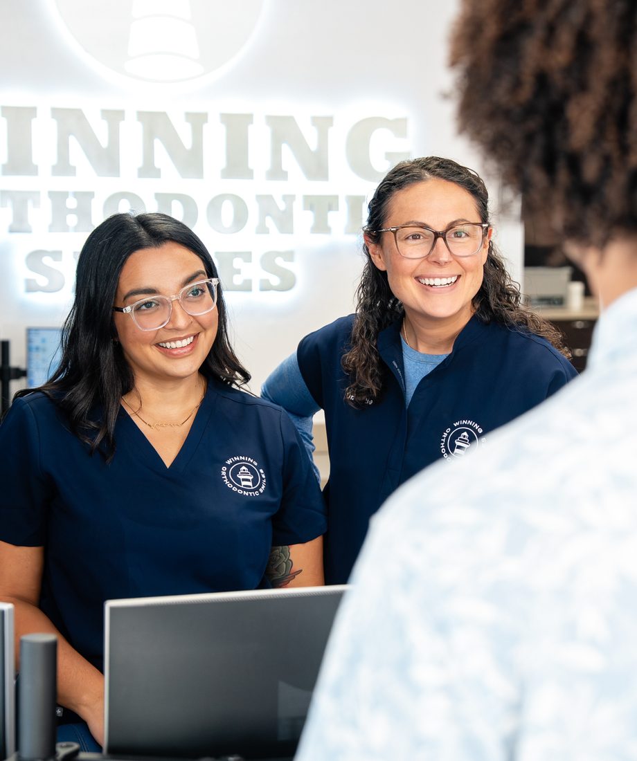 Two Winning Orthodontic Smiles team members smiling with a patient at the front desk