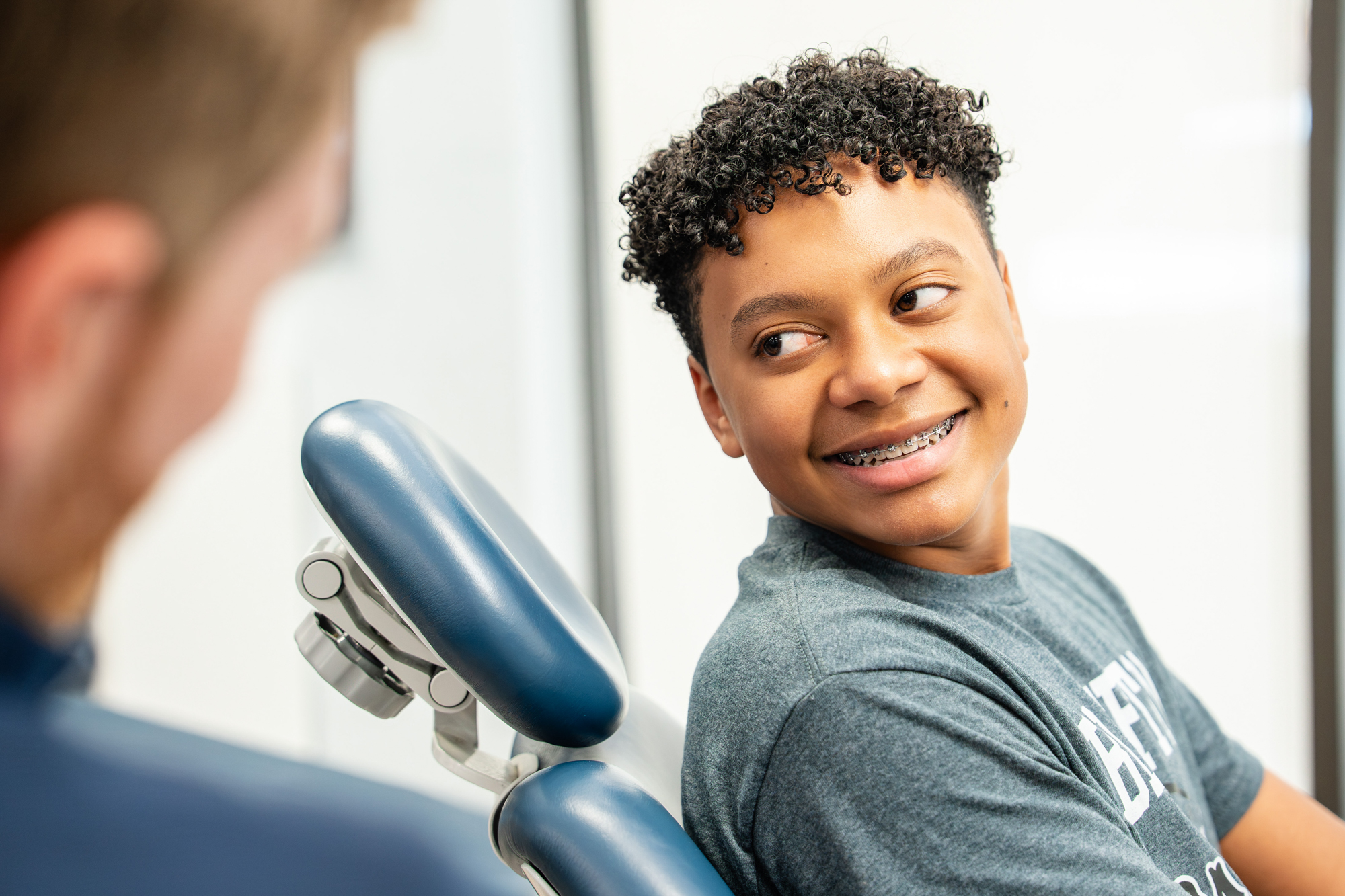 Smiling teen patient in the orthodontic chair talking with his orthodontist