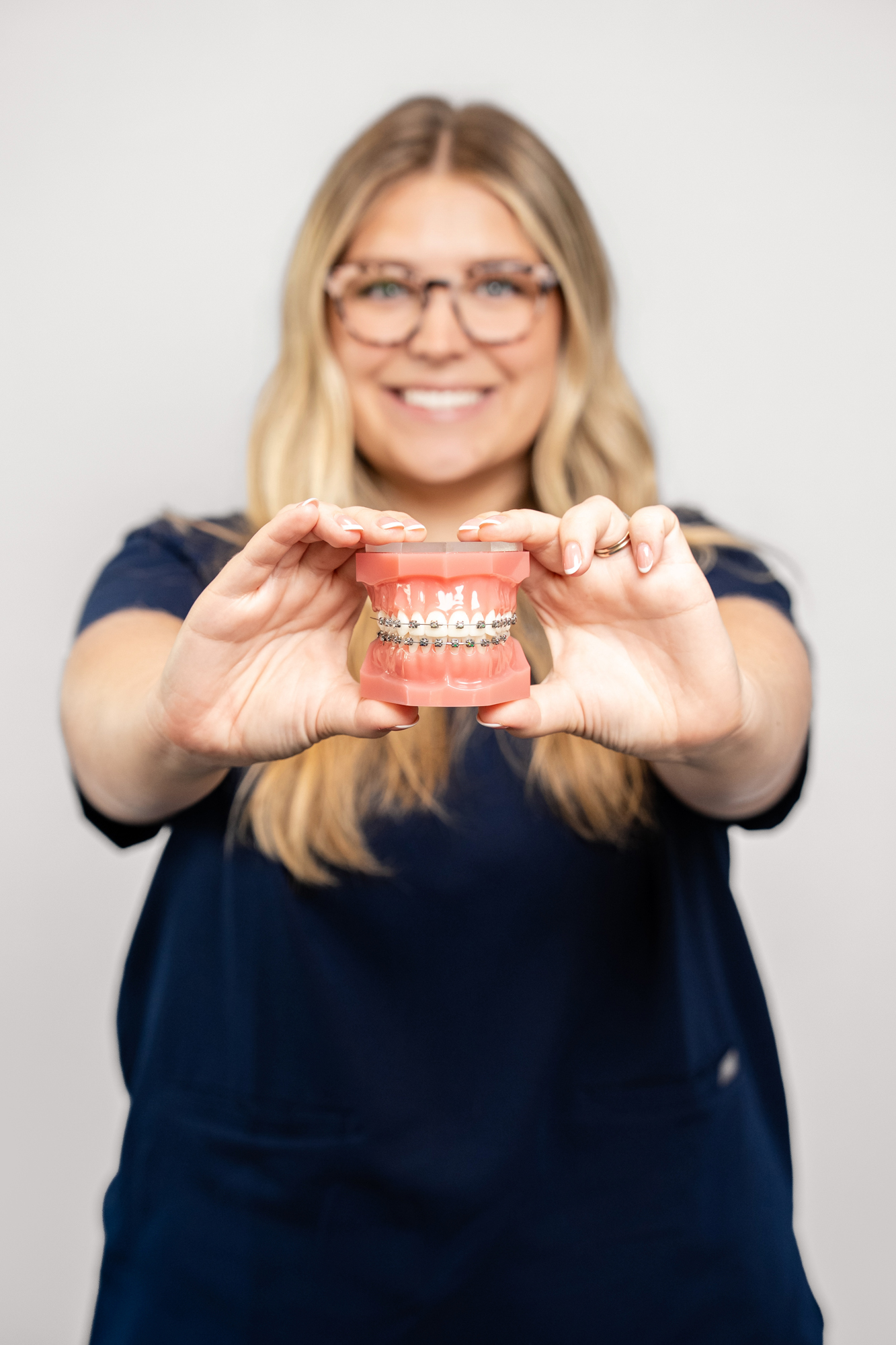 Smiling team member holding a model of teeth with metal braces
